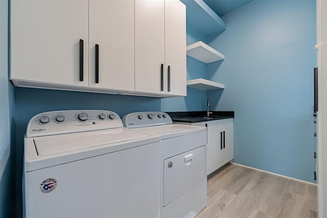 laundry area featuring cabinets, separate washer and dryer, sink, and light wood-type flooring