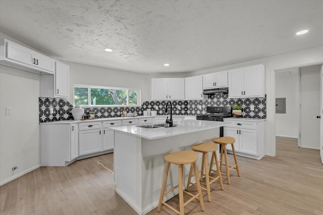 kitchen featuring a kitchen bar, sink, a kitchen island with sink, light hardwood / wood-style floors, and white cabinets