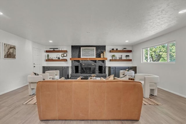 living room with light hardwood / wood-style floors, a brick fireplace, and a textured ceiling