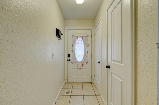 doorway to outside with light tile patterned floors, a textured wall, visible vents, and baseboards