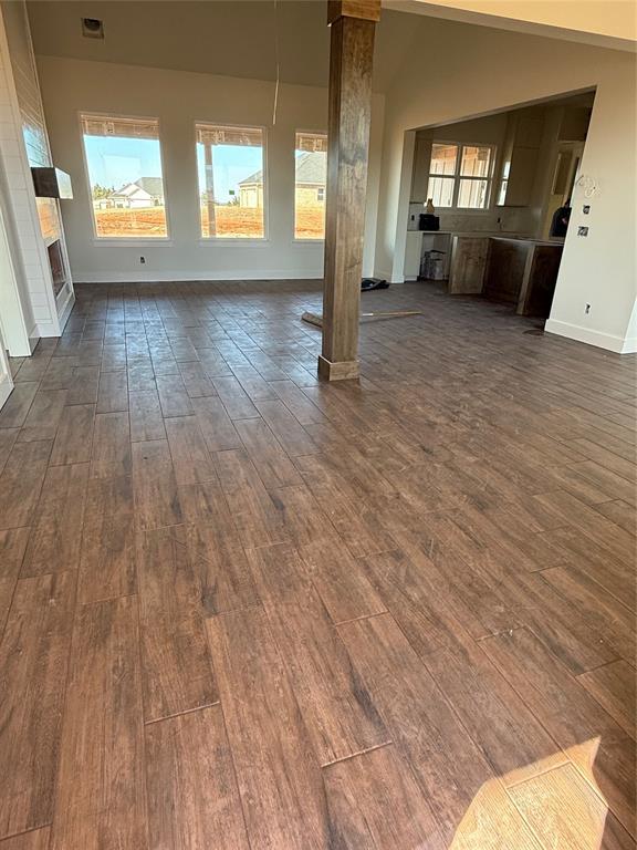 unfurnished living room featuring visible vents, high vaulted ceiling, dark wood finished floors, decorative columns, and baseboards