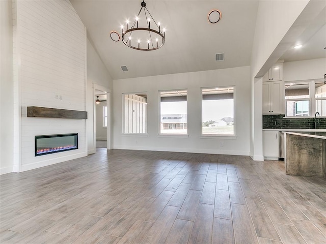 unfurnished living room featuring visible vents, a sink, light wood finished floors, and a notable chandelier
