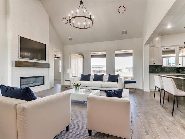 living room featuring a notable chandelier, visible vents, a large fireplace, and light wood-type flooring