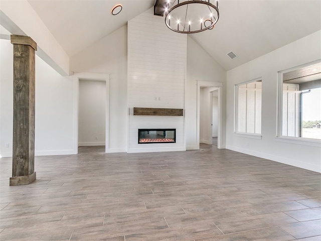 unfurnished living room featuring visible vents, an inviting chandelier, a fireplace, baseboards, and high vaulted ceiling