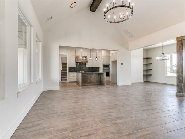 unfurnished living room featuring light wood-style floors, visible vents, beam ceiling, high vaulted ceiling, and an inviting chandelier