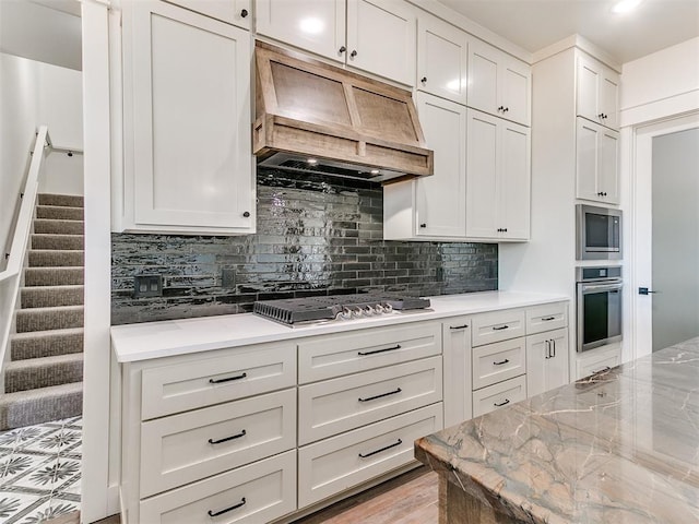 kitchen with decorative backsplash, appliances with stainless steel finishes, premium range hood, and light stone countertops