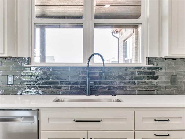 kitchen featuring stainless steel dishwasher, white cabinets, a sink, and tasteful backsplash