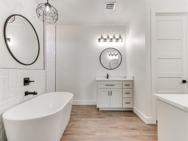 bathroom featuring visible vents, vanity, wood finished floors, baseboards, and a soaking tub
