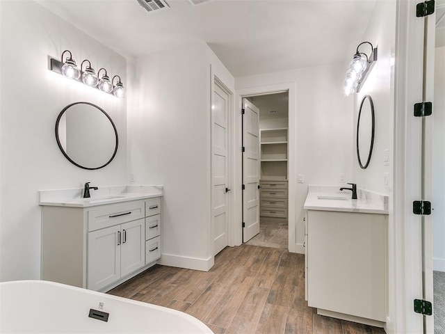 bathroom with baseboards, a sink, two vanities, and wood finished floors