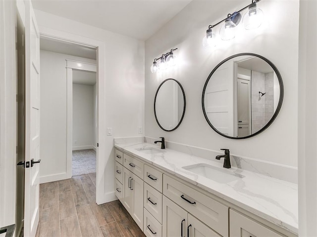 full bath featuring double vanity, a sink, baseboards, and wood finished floors