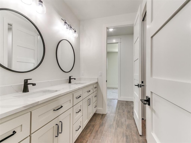 full bath featuring double vanity, a sink, baseboards, and wood finished floors