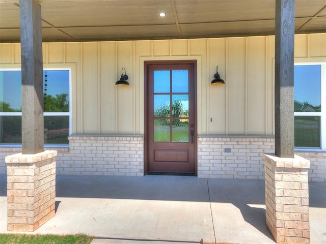 view of exterior entry featuring covered porch, board and batten siding, and brick siding