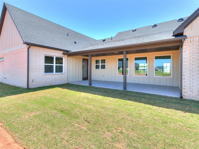 rear view of property with brick siding, board and batten siding, roof with shingles, and a patio area