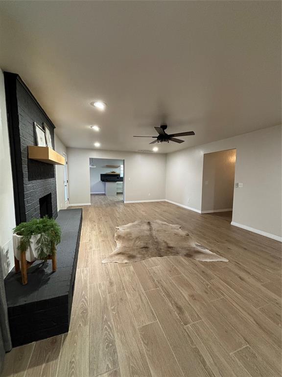 unfurnished living room featuring hardwood / wood-style flooring, a brick fireplace, and ceiling fan