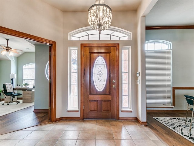 foyer entrance featuring ceiling fan with notable chandelier, a high ceiling, and light tile patterned flooring