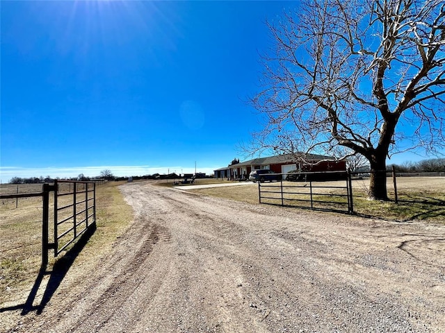 view of street featuring driveway, a gate, a gated entry, and a rural view