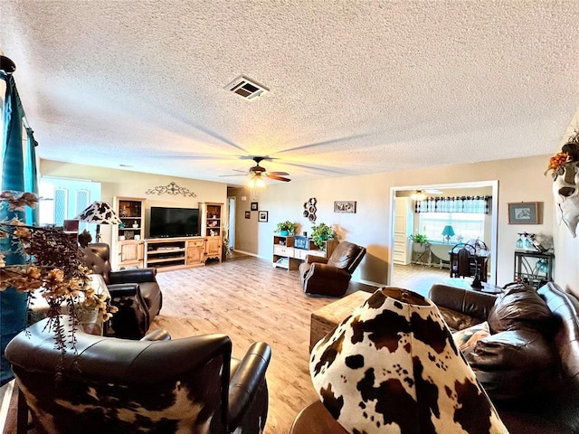 living area with ceiling fan, a textured ceiling, visible vents, and wood finished floors