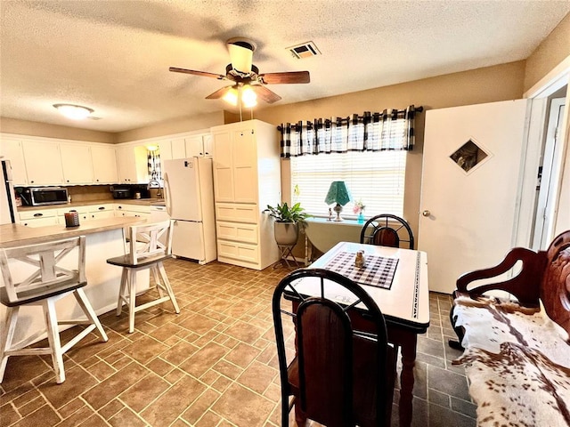 kitchen with visible vents, stainless steel microwave, a kitchen breakfast bar, freestanding refrigerator, and white cabinetry