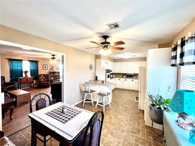 dining room featuring baseboards, a textured ceiling, visible vents, and a ceiling fan