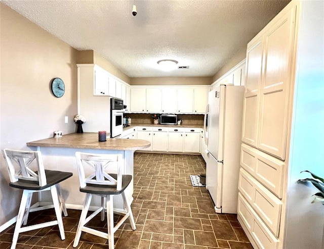 kitchen with visible vents, freestanding refrigerator, white cabinets, a peninsula, and a kitchen breakfast bar