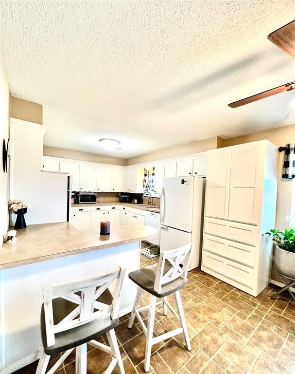 kitchen with a breakfast bar, light countertops, white cabinets, white appliances, and a peninsula