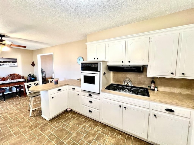 kitchen featuring stainless steel gas cooktop, white cabinets, a peninsula, oven, and under cabinet range hood