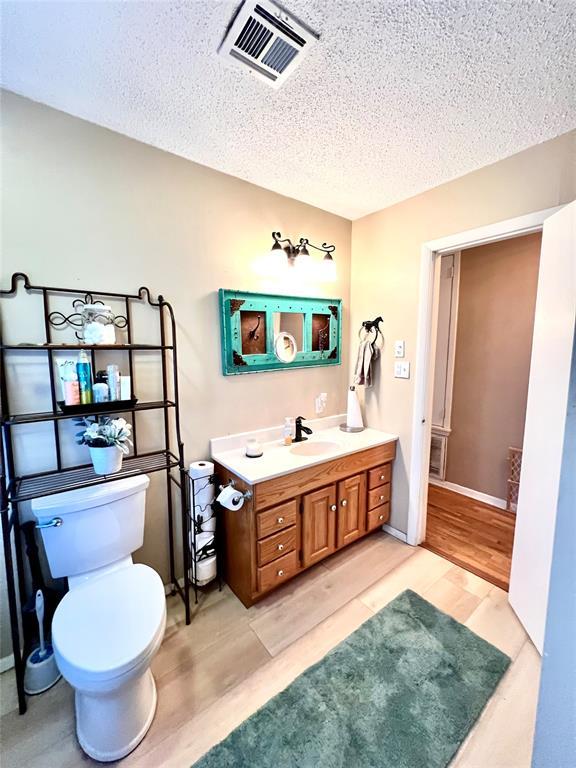 bathroom featuring visible vents, toilet, a textured ceiling, vanity, and wood finished floors