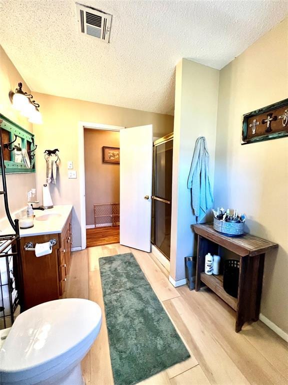 full bath featuring wood finished floors, visible vents, a textured ceiling, a shower stall, and vanity