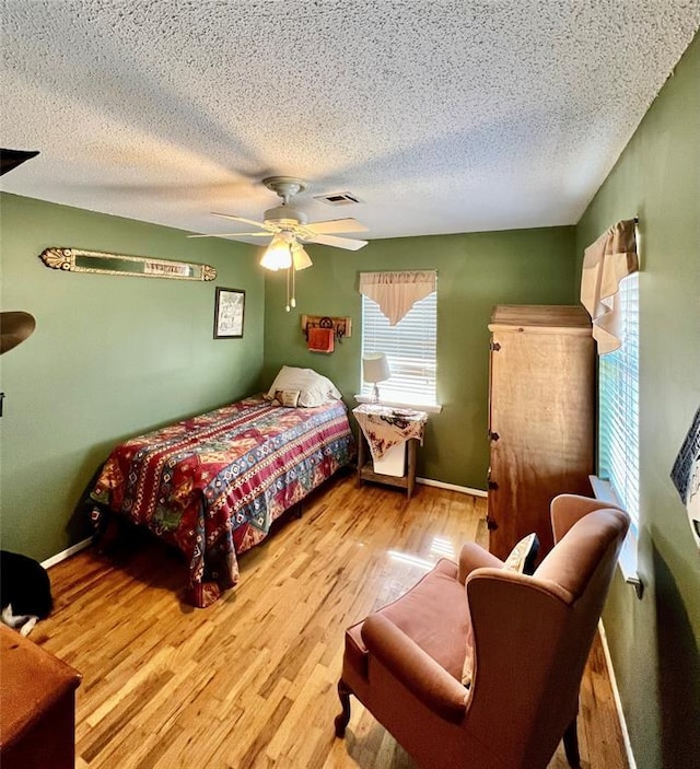 bedroom with ceiling fan, a textured ceiling, visible vents, and wood finished floors