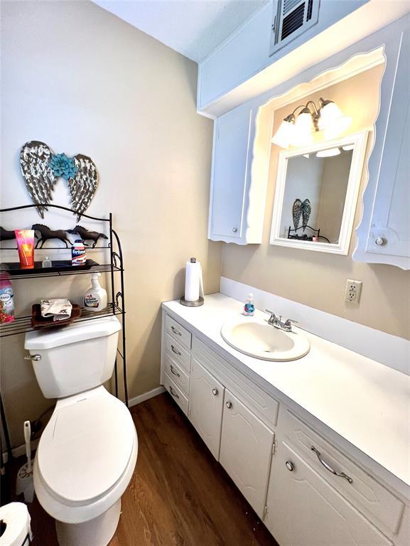 half bathroom with visible vents, toilet, vanity, wood finished floors, and baseboards