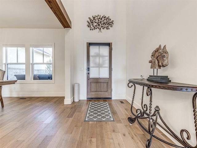 foyer entrance featuring baseboards, beamed ceiling, and light wood finished floors