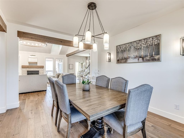 dining room with light wood-style floors, baseboards, and a stone fireplace