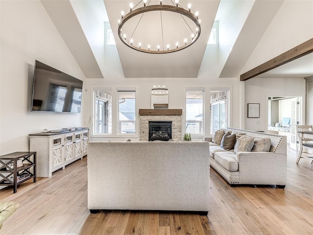 living area featuring high vaulted ceiling, light wood finished floors, a fireplace, and an inviting chandelier