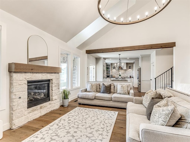 living room featuring stairway, a notable chandelier, a stone fireplace, and wood finished floors