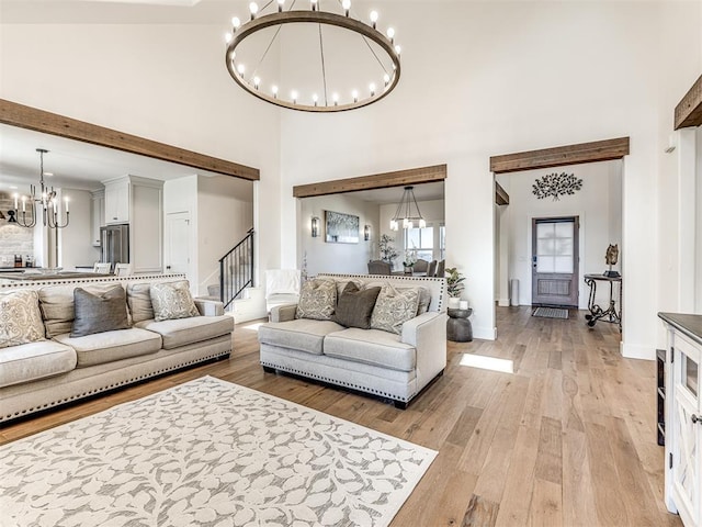 living area featuring baseboards, a towering ceiling, stairs, light wood-style floors, and a notable chandelier