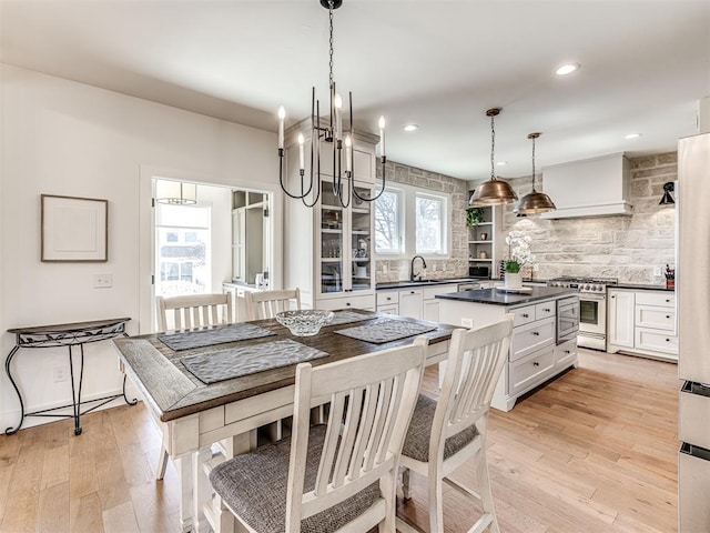 kitchen with decorative light fixtures, dark countertops, custom range hood, white cabinetry, and high end stove