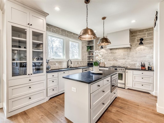 kitchen featuring glass insert cabinets, a kitchen island, white cabinets, stainless steel range, and decorative light fixtures