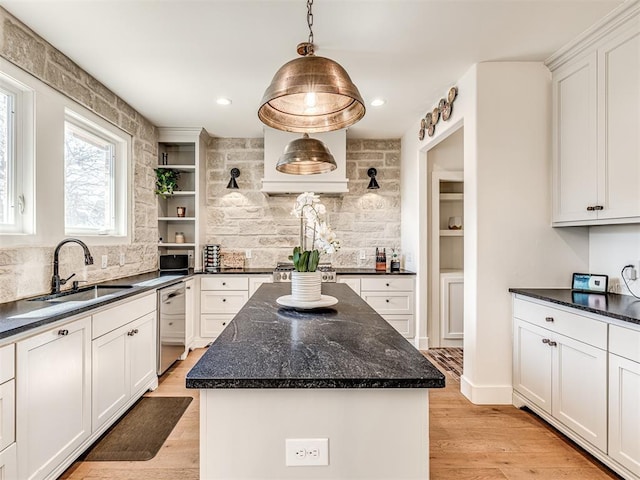 kitchen with a sink, light wood-style floors, white cabinets, hanging light fixtures, and a center island