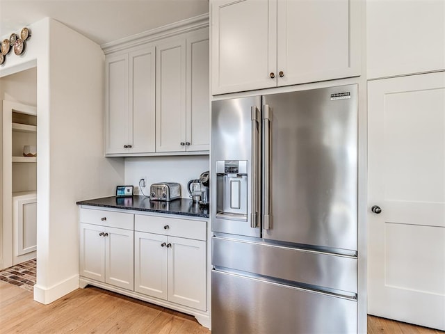 kitchen with high end fridge, light wood finished floors, dark stone countertops, and white cabinets