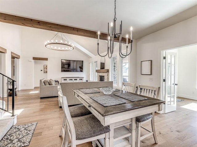 dining area with light wood-style floors, stairway, beam ceiling, and a stone fireplace