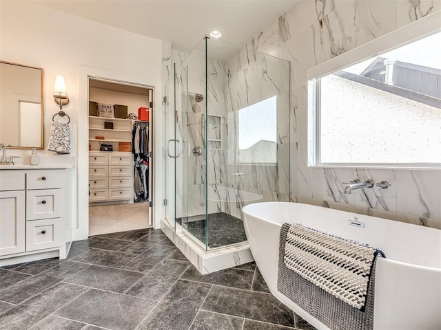 bathroom featuring a freestanding bath, a spacious closet, a marble finish shower, and vanity