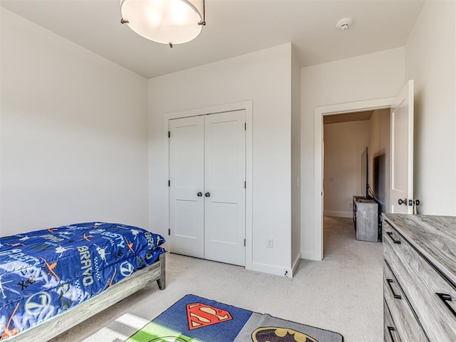 bedroom with a closet, light colored carpet, and baseboards