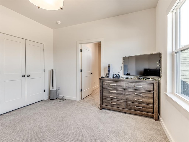 bedroom with multiple windows, baseboards, a closet, and light colored carpet