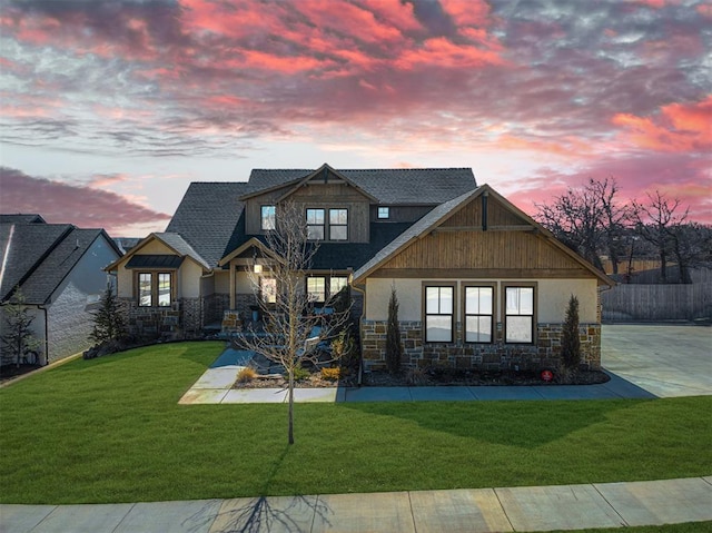 view of front facade featuring a shingled roof, stone siding, driveway, a lawn, and stucco siding