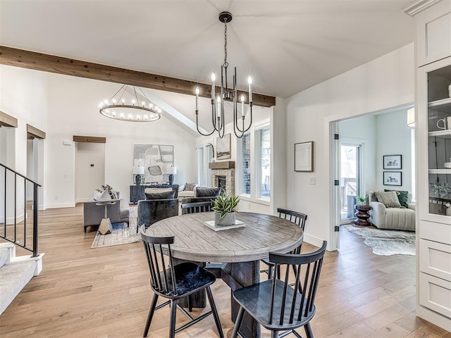 7308 Sunset Sail Ave, Edmond, OK 73034 - dining area with a stone fireplace, stairway, a notable chandelier, vaulted ceiling with beams, and light wood-style flooring