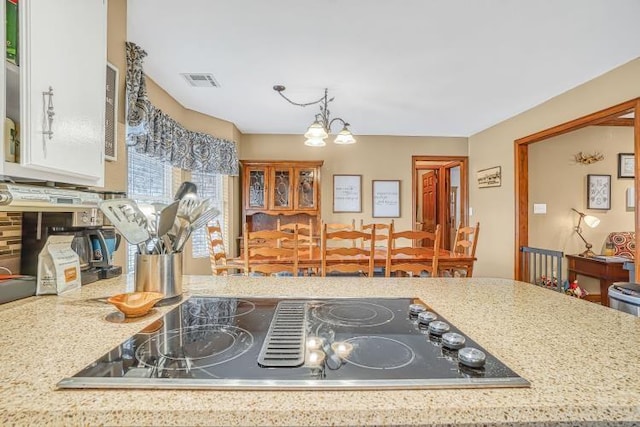 kitchen with decorative light fixtures, black electric stovetop, a notable chandelier, and light stone countertops