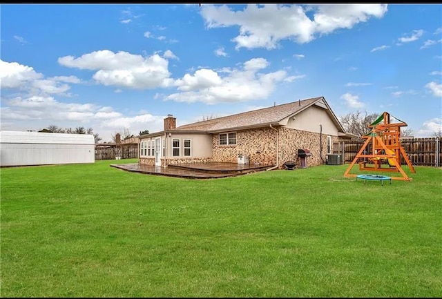 back of house with central AC unit, a yard, and a playground