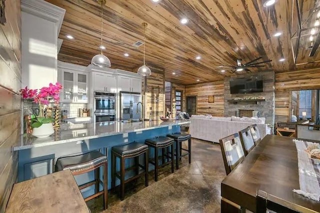 kitchen with decorative light fixtures, white cabinetry, appliances with stainless steel finishes, a kitchen bar, and glass insert cabinets