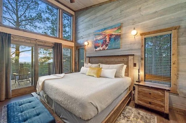 bedroom with a towering ceiling, wood walls, access to exterior, and wood finished floors