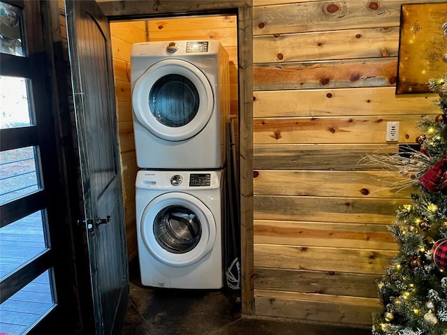 clothes washing area with laundry area, stacked washer / dryer, and wood walls